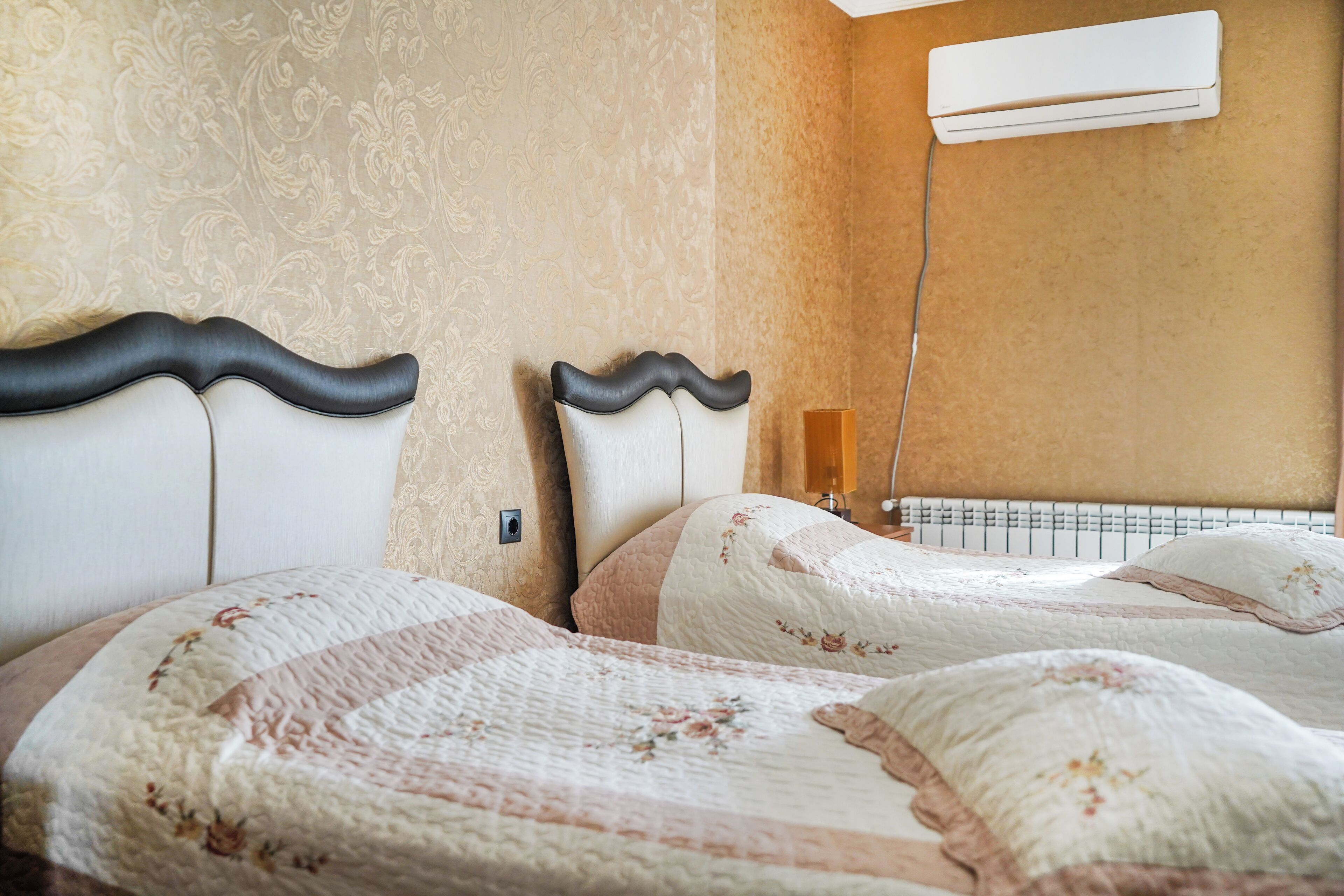 A hotel room with two beds, a wall-mounted air conditioner, and a patterned wall.