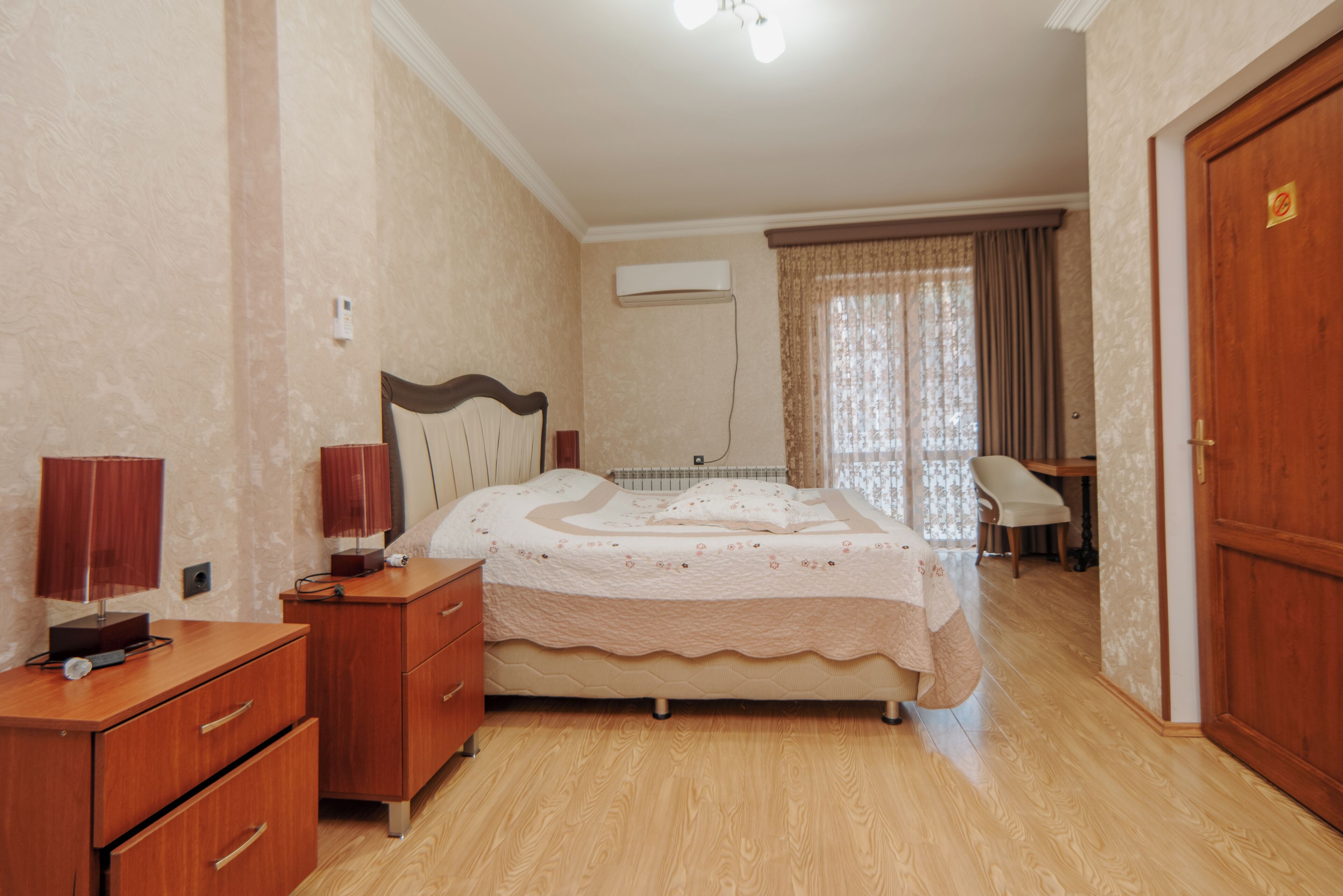 A bedroom with a bed, a nightstand, a dresser, a chair, and an air conditioning unit.