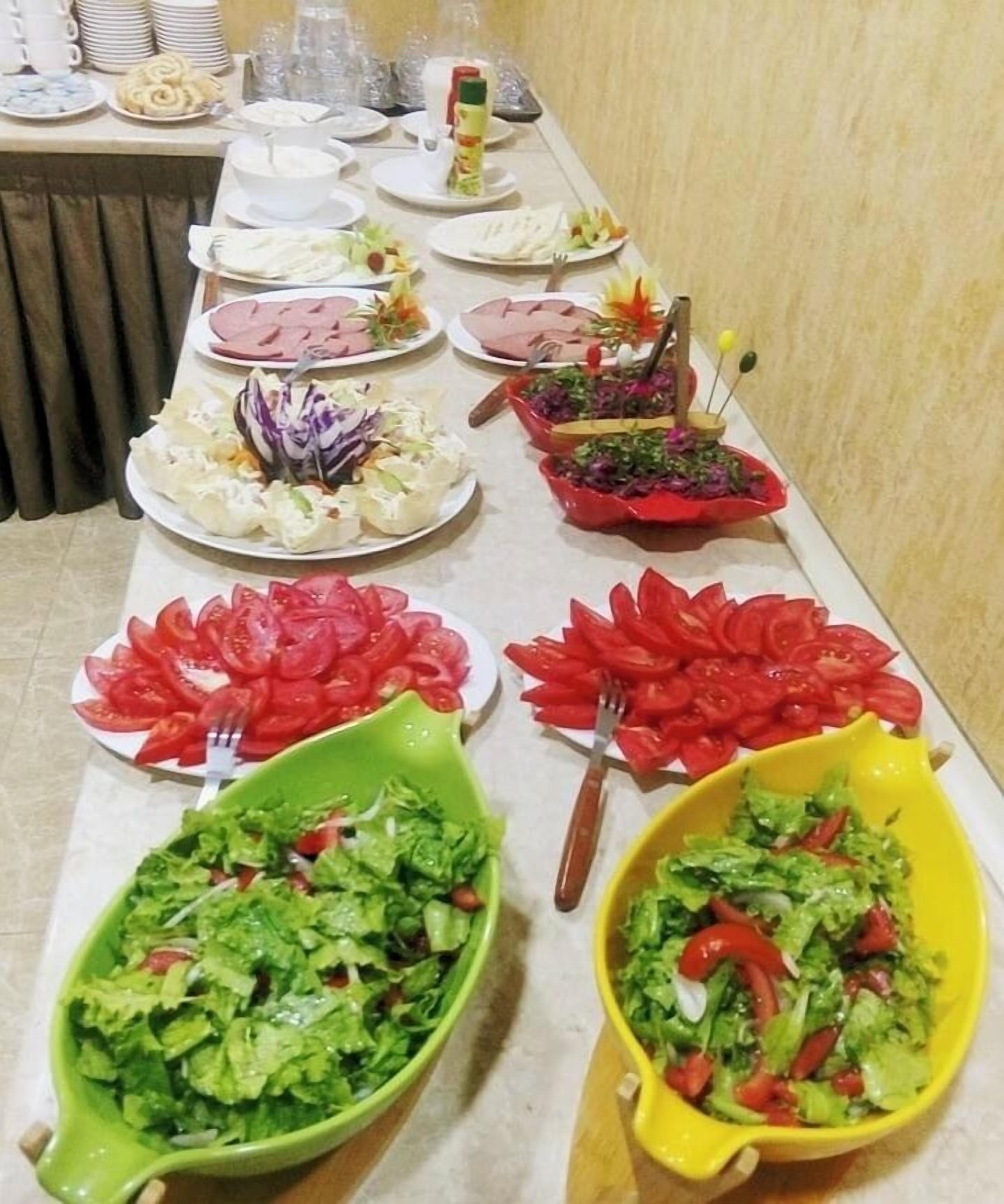 A buffet table with various dishes including salads, sliced tomatoes, and meat.
