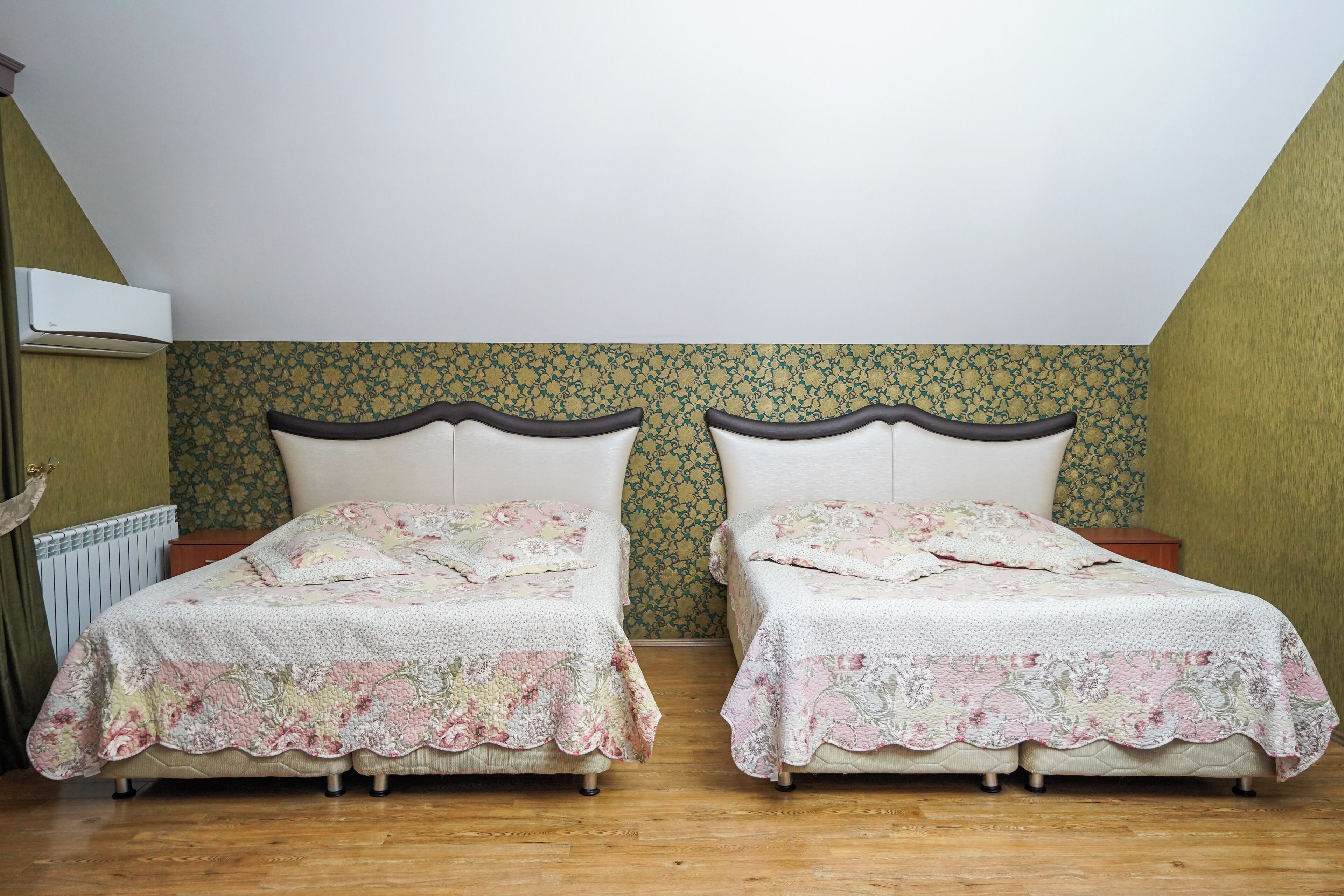 A room with two beds, each with floral bedding, a radiator, and patterned wallpaper.