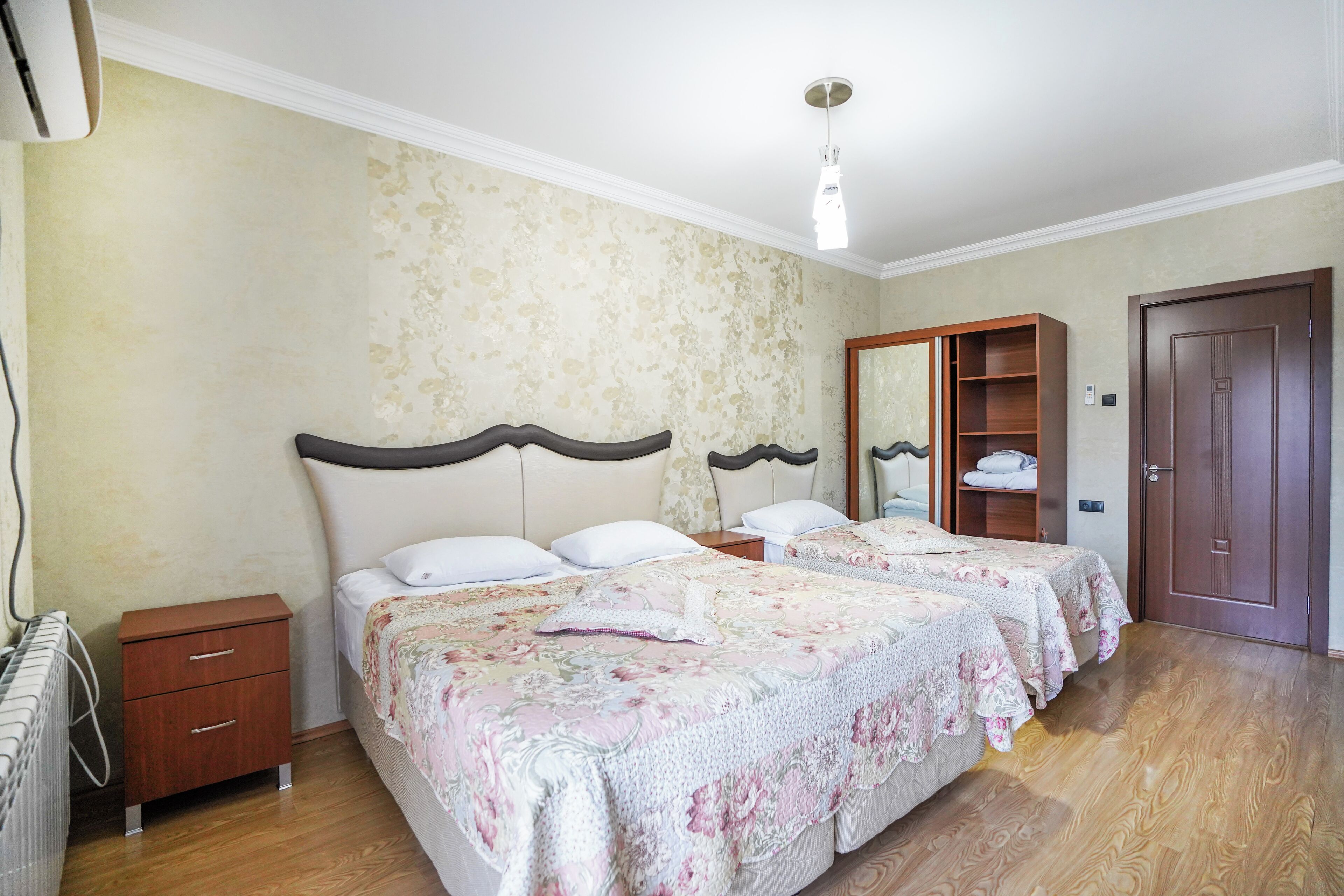 Un dormitorio con dos camas, un armario de madera, una mesita de noche y un radiador.
