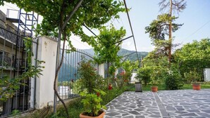A stone-tiled patio with potted plants and a view of mountains. - Natali Hotel (Borjomi)