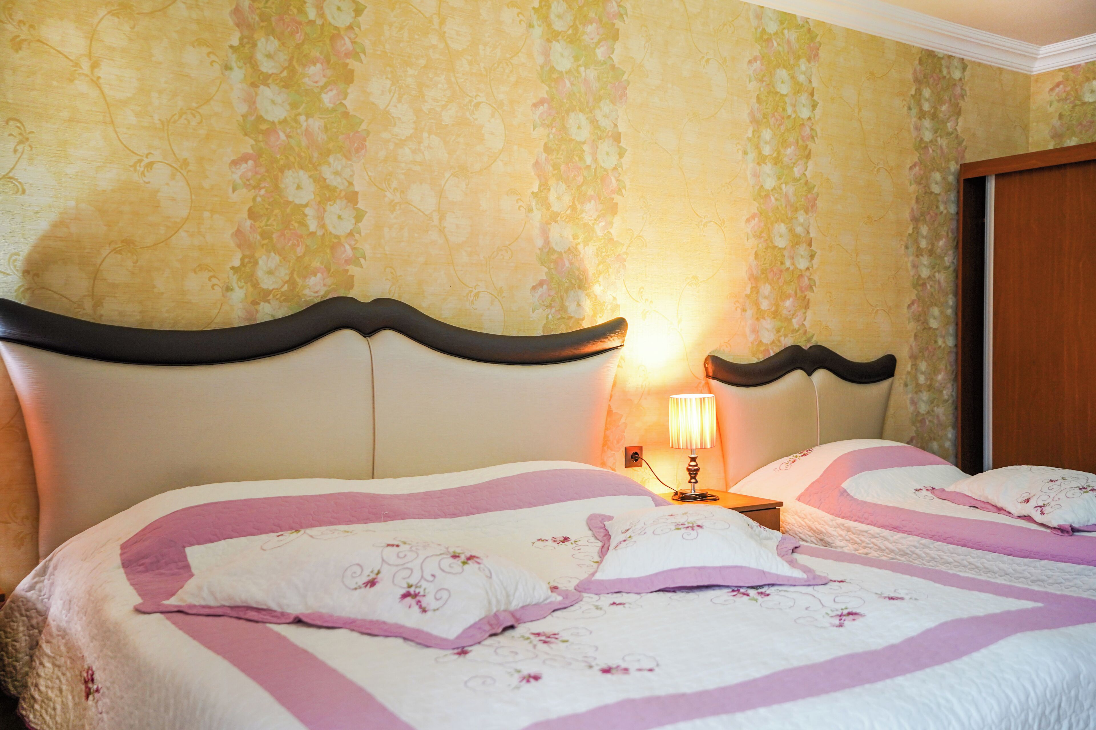 Habitación de hotel con dos camas, papel tapiz floral y una mesita de noche con lámpara.