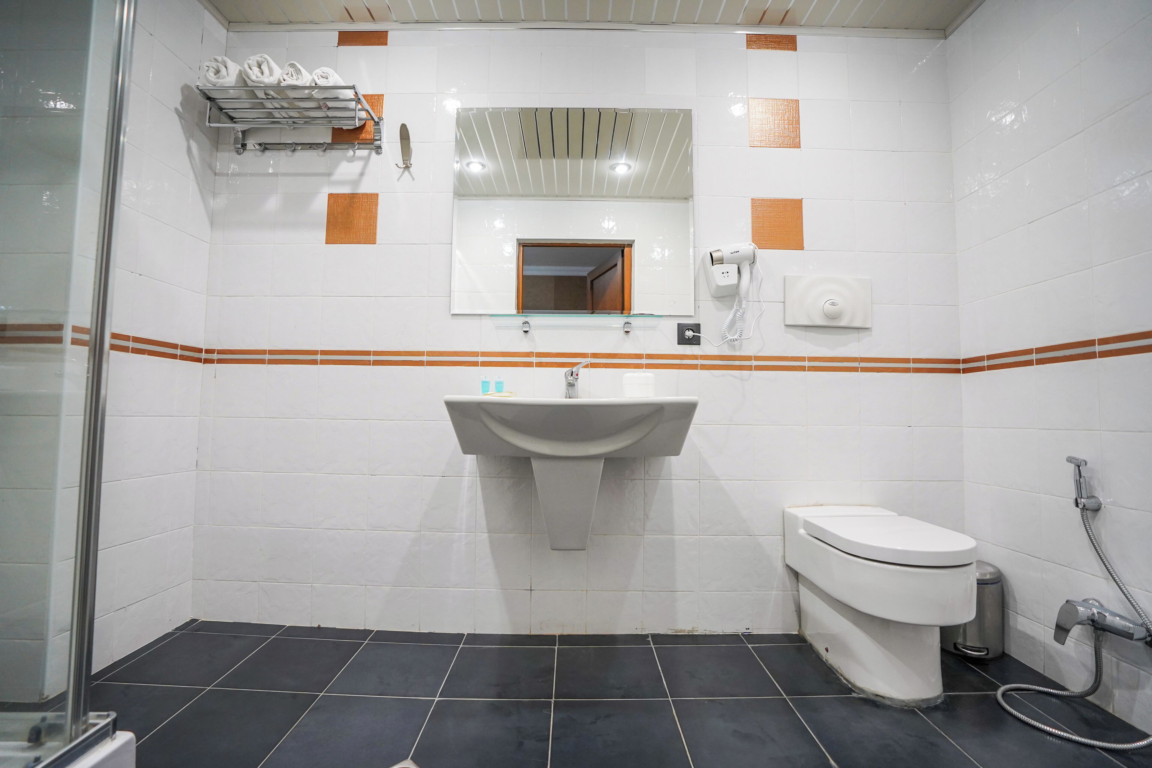 A bathroom with a sink, toilet, and shower. There is a mirror above the sink and a towel rack with towels.