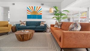 A modern living room with a blue sofa, an orange sofa, a wooden coffee table, and a large plant. - Sunset Retreat| Pool Oasis,Walk to Beach,Billiards (Redington Beach)