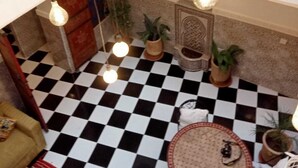 A checkered floor, a round table with chairs, hanging light bulbs, and a blue railing. - Riad L'ayinn in Marrakesh (Marrakech)