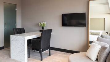 A modern hotel room with a marble desk, black upholstered chairs, a flat-screen TV, a large mirror, and a sofa with multiple cushions.