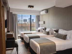 Quarto de hotel com duas camas, uma escrivaninha, televisão e uma janela grande com vista para a cidade.