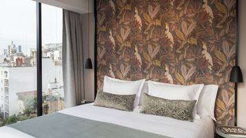 Ein Hotelzimmer mit einem großen Bett, Blick auf die Stadt und einer Wand mit tropischem Blattmuster.