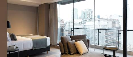 Una habitación de hotel moderna con un ventanal grande, una cama, un sofá y una mesita.