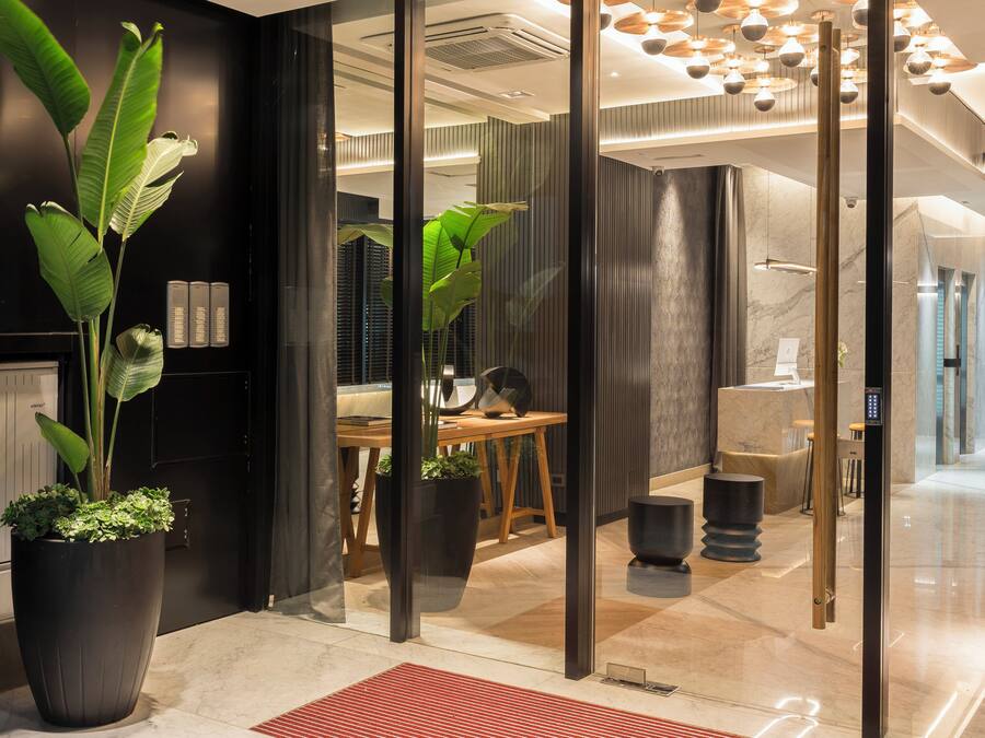 Um interior moderno com um balcão de recepção, plantas em vasos e um tapete vermelho na entrada.