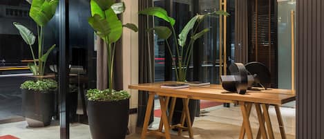Un interior moderno con una mesa de madera, plantas en macetas y un gran ventanal con persianas.