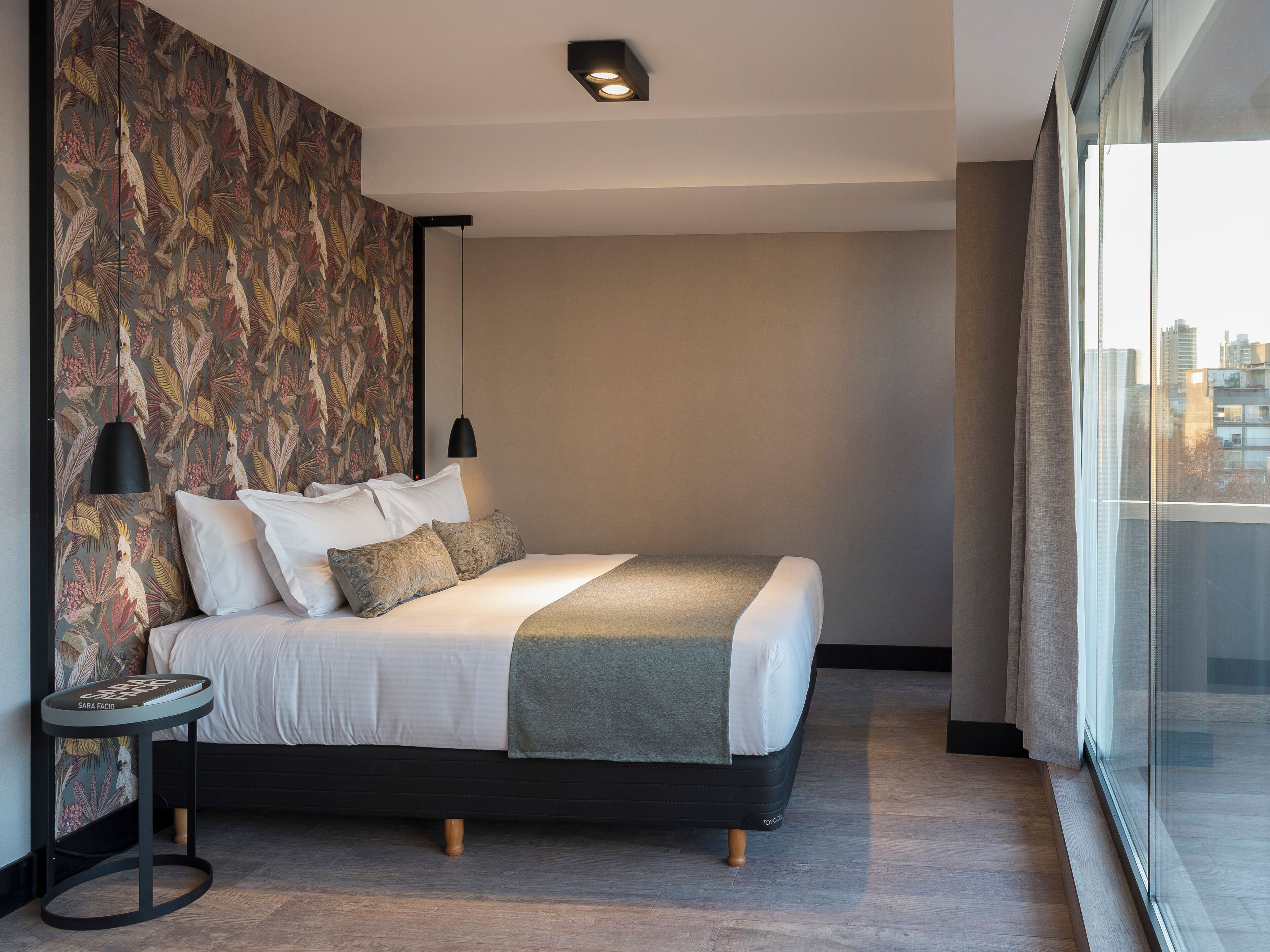 A modern bedroom with a large bed, a side table, and a city view through the window.