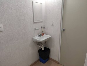 Une petite salle de bain avec un lavabo blanc, un miroir et une poubelle noire.