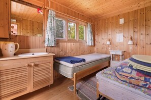 A wooden cabin room with a bed, a small bedside table, a window with curtains, a sink, and a mirror. - Cabin - Sleeps 6 - Pets Ok - Pato - Parking (Meloy)