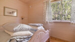 Una habitación de madera con una cama, un cuadro enmarcado en la pared y una ventana con cortinas florales.