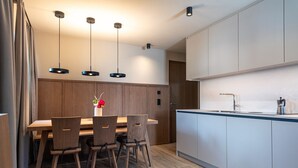 Une cuisine moderne avec une table et des chaises en bois, des luminaires suspendus et un îlot central intégré doté d’un évier.