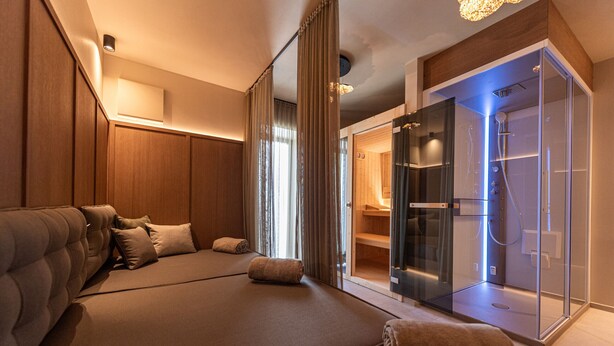 Une chambre d’hôtel moderne dotée d’un grand lit, d’un dressing et d’une douche séparée par des parois en verre.