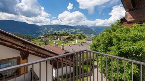 Un balcon offrant une vue sur un village, des montagnes et un ciel dégagé.