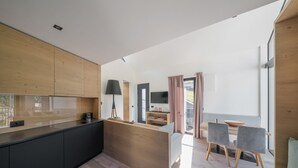 Una cocina moderna con una isla de madera, un comedor con mesa y sillas, y un espacio de estar con televisor y cortinas.