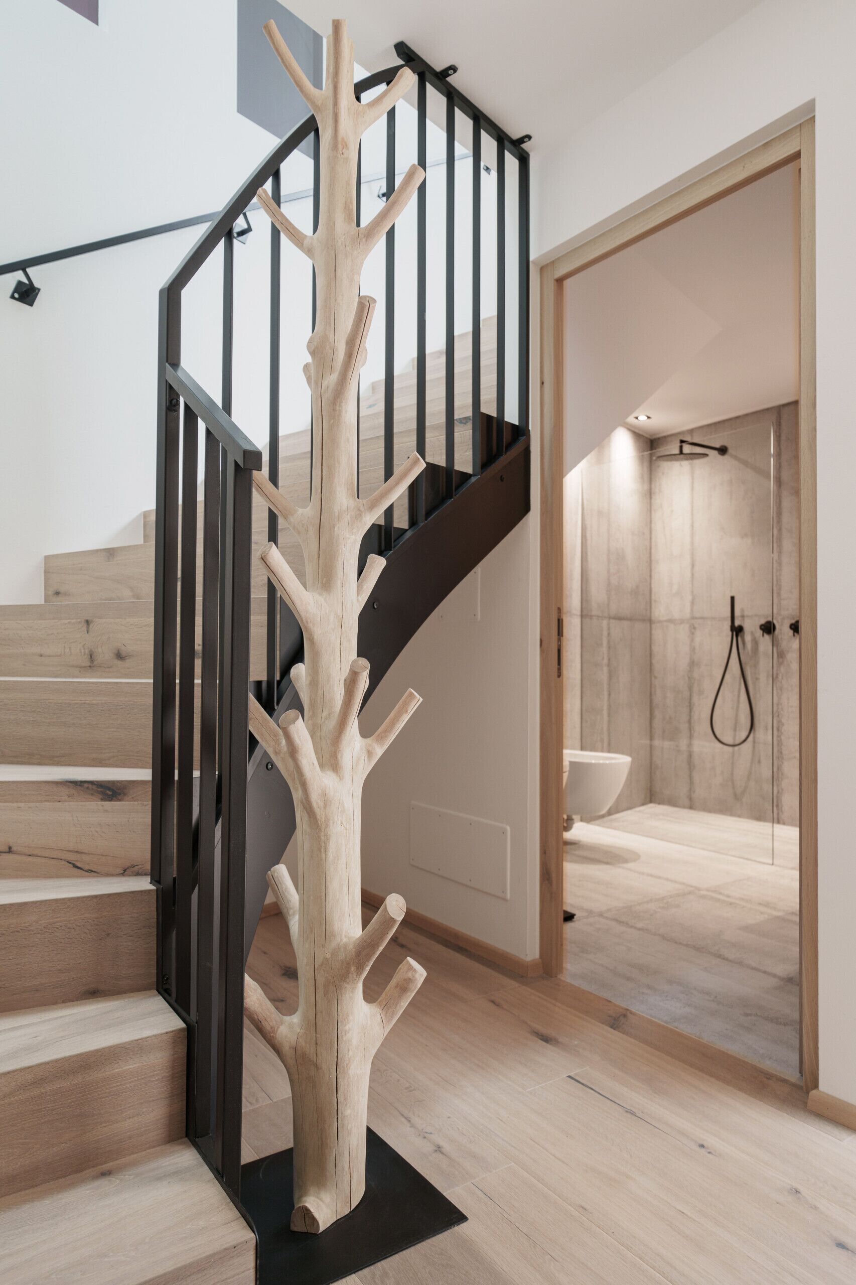Un escalier moderne agrémenté d’une sculpture en bois originale, d’une rampe noire et d’un espace douche avec un mur en marbre.