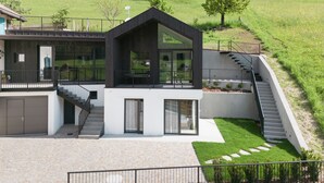 Una casa moderna de dos pisos con balcón, una escalera que lleva a un segundo nivel y un césped bien cuidado.