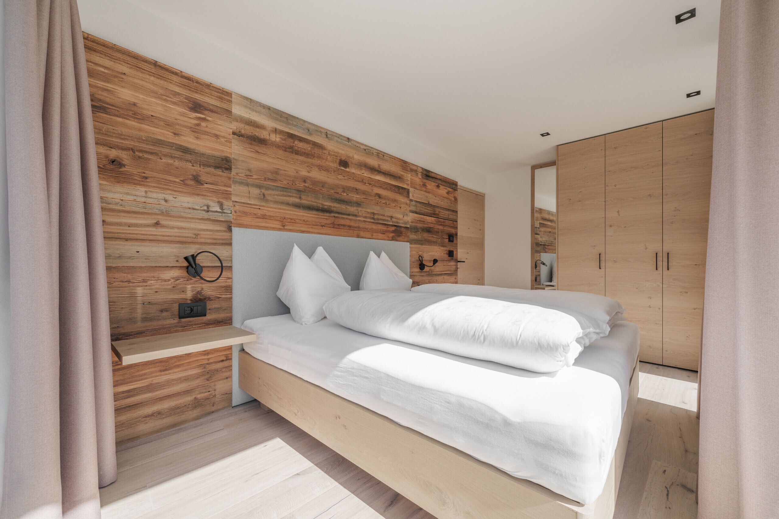 Une chambre à coucher moderne avec une tête de lit en bois, un lit recouvert de linge de maison blanc, une table de chevet et une armoire.