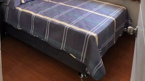 Un lit bien fait, recouvert d’une couvre-lit à rayures bleues et blanches, avec une tête de lit sombre et une fenêtre ornée de rideaux bruns.