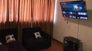 Un salon avec deux canapés sombres, un téléviseur à écran plat fixé au mur et une petite table.