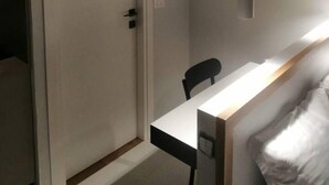 A room with a white door, a desk with a chair, and a hanging light fixture.