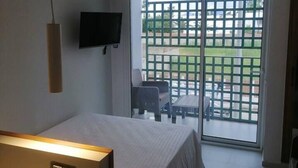 A hotel room with a bed, a TV mounted on the wall, a desk with a lamp, and a view of the outside balcony.