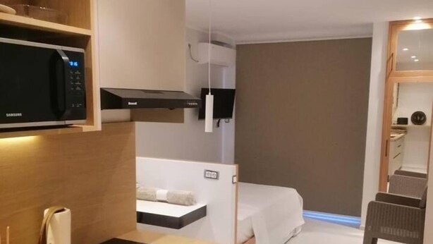 A modern hotel room with a kitchenette, a bed, and a seating area.