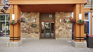 En lodges indgang med stenvægge, et træudhæng og blomsterkasser hængende under taget.
