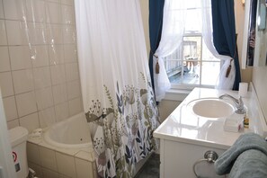 A bathroom with a bathtub, a sink, and a window with curtains. - The 87th House (Portland)
