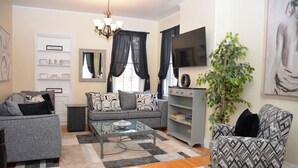 A living room with a sofa, armchair, coffee table, TV, bookshelf, and a plant. - The 87th House (Portland)
