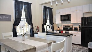 A modern kitchen with white cabinets, a black refrigerator, and a dining area with a table and chairs. - The 87th House (Portland)