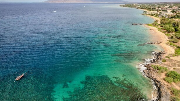 Vista costera con aguas turquesas cristalinas, un barco y montañas al fondo.