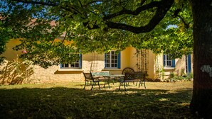 En innergård med ett bord och stolar, omgiven av en gul byggnad med blåa fönsterluckor.