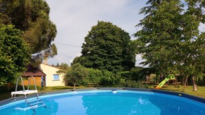 En swimmingpool med ett kaklat poolområde, omgiven av träd och en liten byggnad.