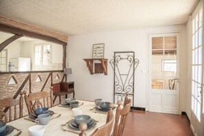 A dining area with a wooden table set for four, surrounded by chairs. There is a white door with glass panels and a window on the right.