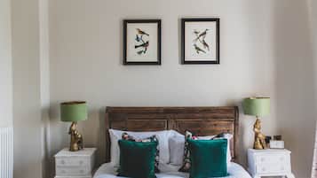 Une chambre à coucher avec une tête de lit en bois, deux illustrations d’oiseaux encadrées au mur, un lit avec des coussins verts et deux tables de chevet avec des lampes.