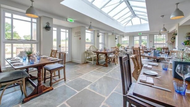 A spacious dining area with high ceilings and large windows, featuring wooden tables and chairs, and a skylight. - The Kedleston Country House (Derby)