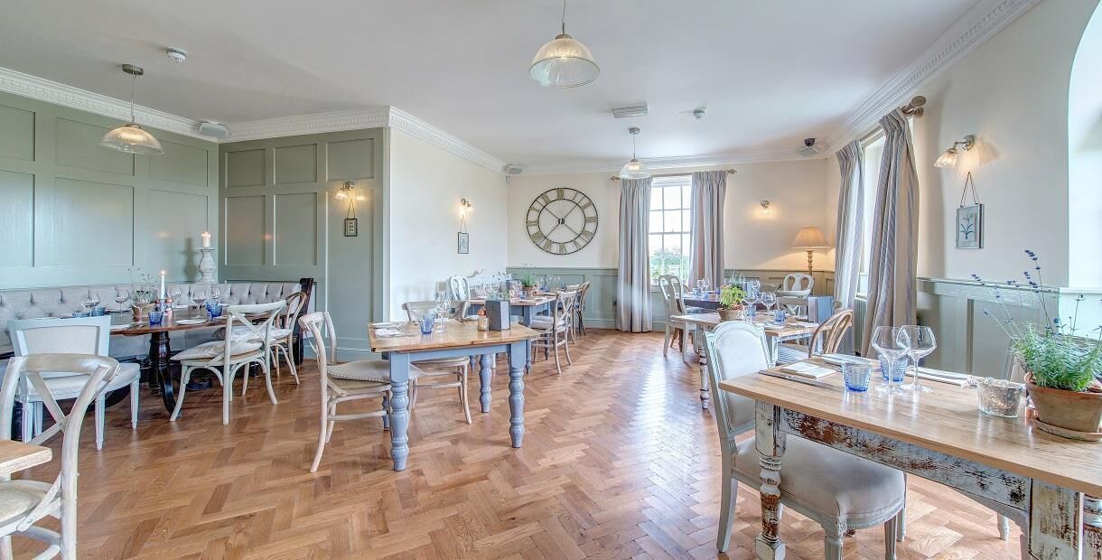 A spacious dining area with wooden flooring, multiple tables, and chairs.