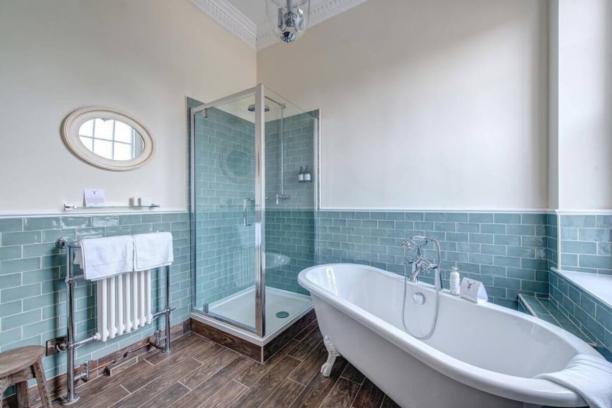 Un baño con ducha de vidrio, una bañera independiente y un perchero con toallas blancas.