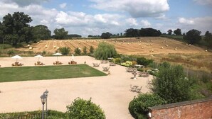 A rural landscape with a field of hay bales, a sandy area with outdoor seating, and a brick wall. - The Kedleston Country House (Derby)