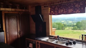Une cuisine rustique avec des meubles en bois, une cuisinière encastrée et une grande fenêtre donnant sur un paysage verdoyant.