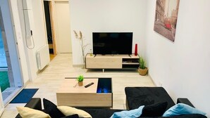A modern living room with a flat-screen TV, a wooden coffee table, a black sofa, and a painting on the wall.