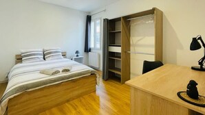 A bedroom with a bed, bedside table, desk, chair, wardrobe, and a window with curtains.