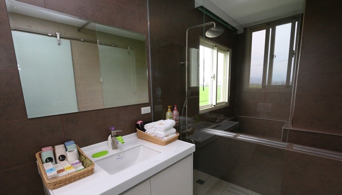 A modern bathroom with a large mirror, a shower, and a sink. There are toiletries and towels on the counter.