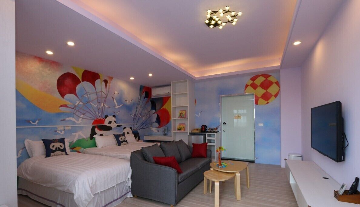 A modern bedroom with a bed, a sofa, a TV, and a colorful mural on the wall.